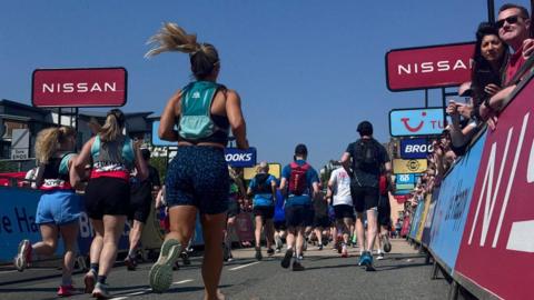 People running down the road while spectators watch from behind the partition