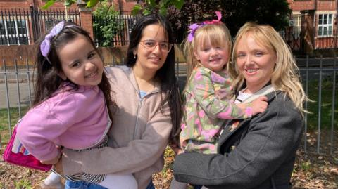 Two mums and their daughters are smiling for the photo in a park near the Saffron pre-school in Leicester. 