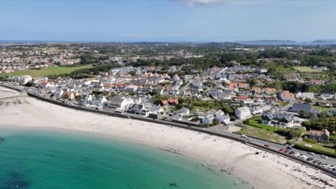 An aerial view of Guernsey with the sea on the left-hand corner and houses on the right hand corner.