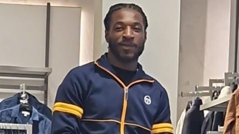 Shaquille Graham wearing a zip-up jumper in navy blue with yellow details.