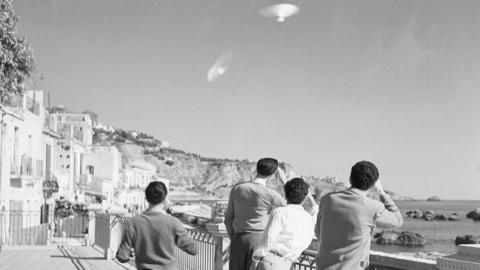 Black and white image of a group of people looking into the sky at a UFO