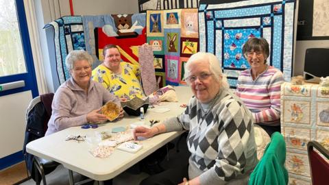 Four members of the sewing club making various items. The women are sitting around a table.