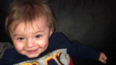 Ethan, a smiling young boy with dark hair, wearing a blue, grey and red jumper that says "Play" on it. 