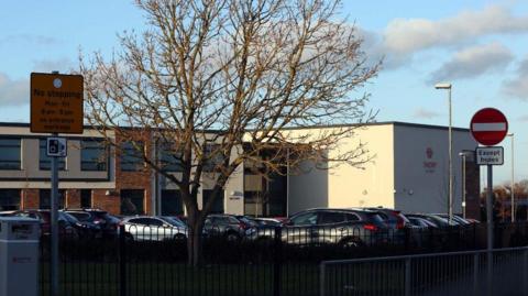 Exterior of Throp Academy in Ryton, Gateshead. There are many cars parked outside a large white building. 