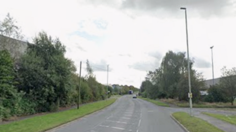 A Google Streetview of Regs Way. Industrial units and trees can be seen either side of the road.