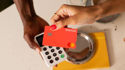 An image of a bright pink monzo card being tapped on a small handheld card reader