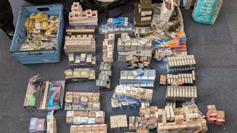 Hundreds of packets of cigarettes and tobacco laid out in piles on an office carpet. 