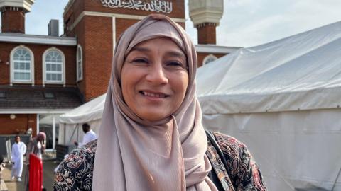 Farkhanda Muneer is wearing a headscarf and is stood in front of the mosque.
