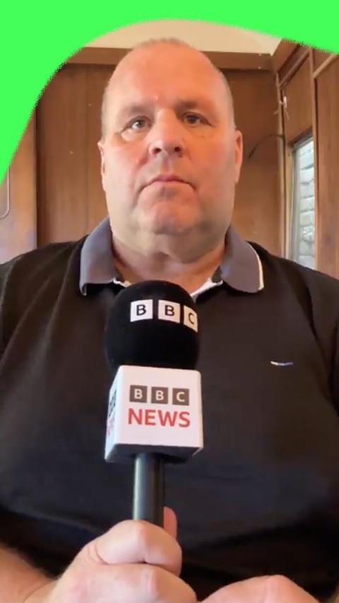 Big John, wearing a black polo top with a light grey collar, hold a BBC microphone.