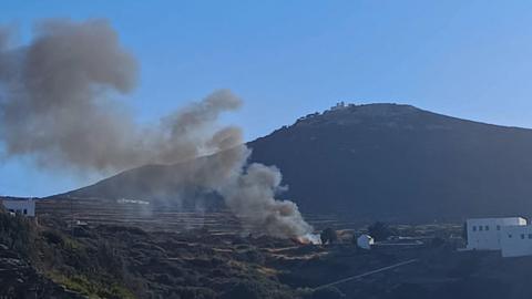 Large plume of grey smoke seen coming from a crash site, with a large mountain in the background