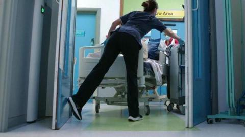A nurse wheels a patient's bed down a hospital corridoor