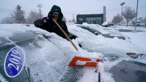 A worker clears cars of snow at the Bereg used car lot after an overnight storm in Orem, Utah