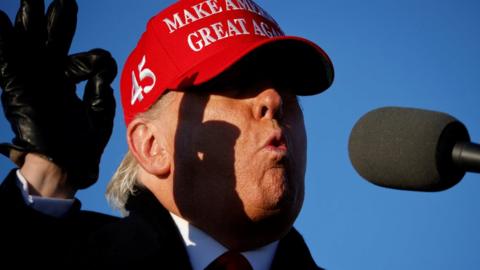 Donald Trump raises his hand in an ok gesture, wearing a coat hat and gloves in Pennsylvania