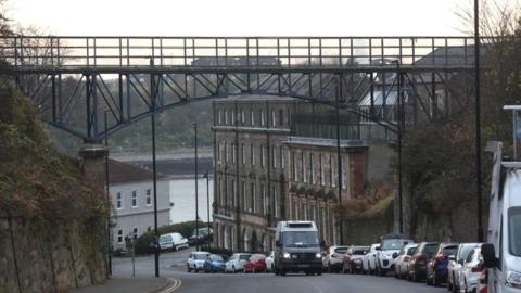 A van drives beneath a high metal footbridge