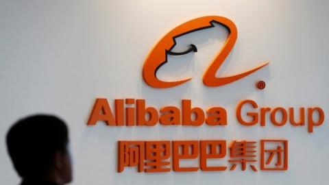 A man stands near the logo of Alibaba Group at the company"s newly-launched office in Kuala Lumpur