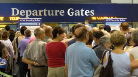 Passengers standing by an airport departure gate sign