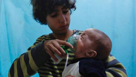 A Syrian boy holds an oxygen mask over the face of an infant
