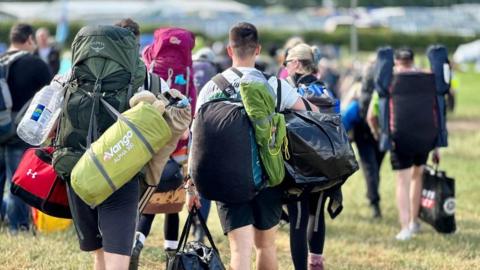 People walking into the festival shown from behind, carrying big rucksacks