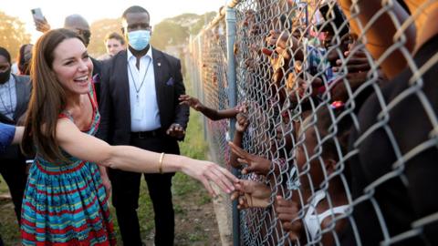 The Duchess of Cambridge reaches out to a child through a metal fence