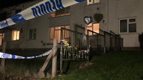 A house with police cordon and floral tributes