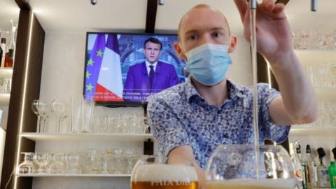 A man pours a beer in a bar while President Macron is on the TV behind him.