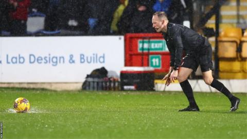 The referee tries to roll the ball on the pitch before calling off the match