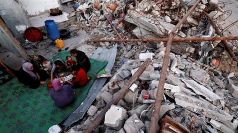 Palestinians eat a meal amid the rubble of their destroyed home in Rafah, in the southern Gaza Strip (13 March 2024)
