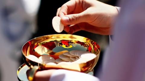 A priest holds a Holy Communion wafer as Pope Benedict XVI celebrates Mass at Nationals Park April 17, 2008 in Washington, DC