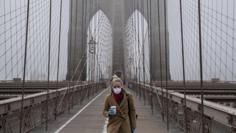 A woman wearing a mask walks the Brooklyn Bridge on 20 March 2020 in New York City