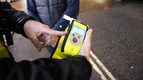A police officer holding a breathalyser