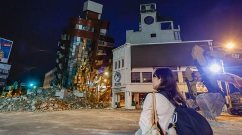 A woman looks at the wreckage of a partially collapsed residential building following the earthquake in Hualien