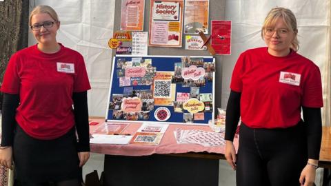 Katie Poyner and Harriet both standing in front of the History Society freshers fayre stall