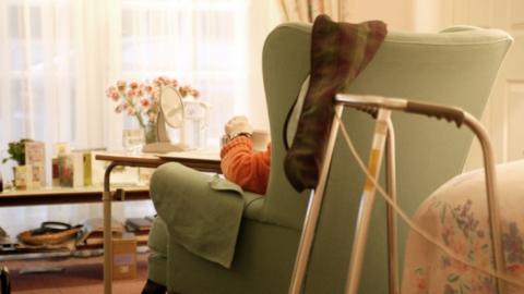 A woman sitting in an armchair inside a care home