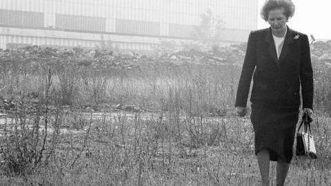 Margaret Thatcher walking through a derelict site