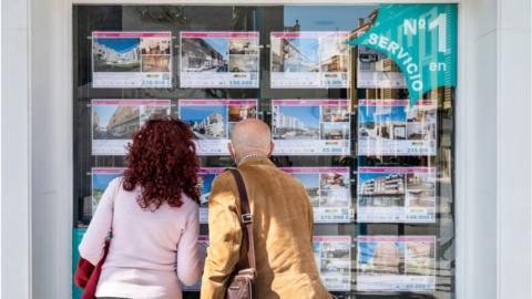 Two people peer into a real estate property agent window