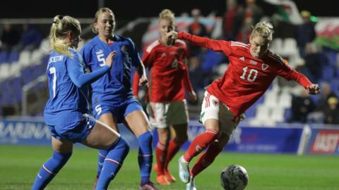 Jess Fishlock dribbles the ball away from two Iceland defenders