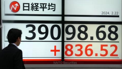A person walks past a display showing record high closing of the Nikkei Stock Average in Tokyo, Japan, 22 February 2024.