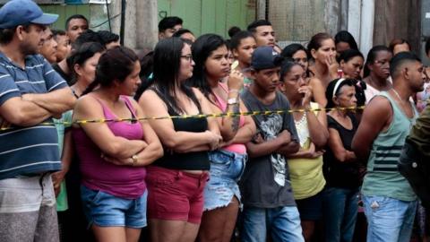 Residents gather outside a bar as forensic personnel and criminal police remove corpses after a shooting, in Belem, Para state, Brazil on May 19, 2019.