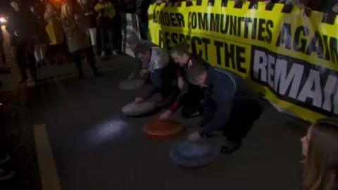 Protesters are banging mental bin lids on a road as part of an anti-Brexit protest.