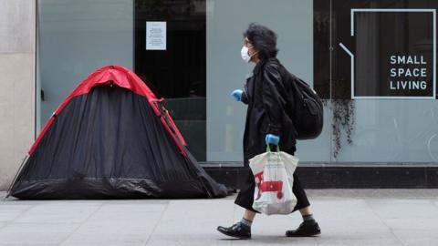 A woman walking past a homeless person's tent erected outside a furniture store