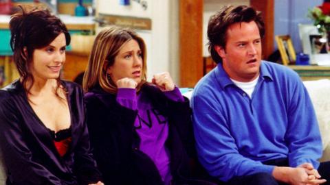 Monica, Rachael and Chandler in Friends, sitting on the sofa reacting
