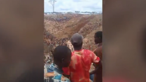 The backs of three men as they look down into a pit at a mining site in the Central African Republic after a landslide
