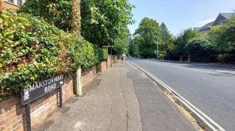 A black and white Marston Ferry Road sign sits in front of an empty run in the sunshine