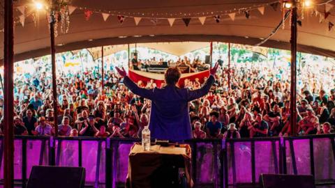 DJ performs in front of crowd at a festival