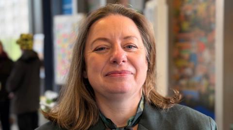 Maria Romero is standing in Reading station wearing a GWR uniform. She has shoulder length brown hair and is smiling at the camera.