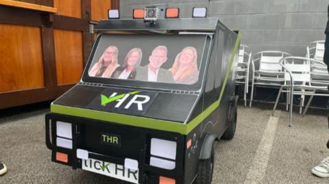 A Tick HR Solutions Ltd soapbox designed like a car in black and green with cutouts of four people in the windscreen