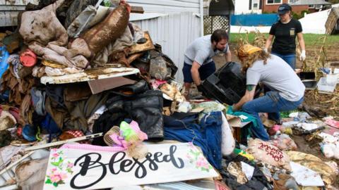 People clean debris near a sign that says "blessed"