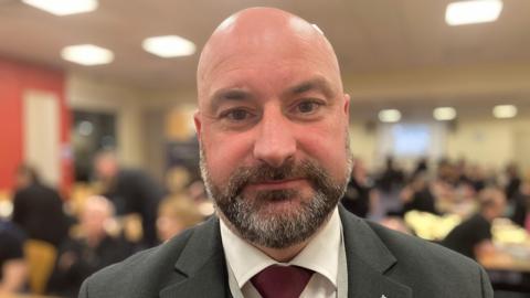 Head and shoulders photograph of Lincolnshire Police and Crime Commissioner Marc Jones. He is bald with a grey and dark brown beard. He is wearing a grey blazer with a white shirt and dark red tie.