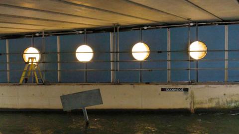 Four circular lights underneath a bridge on Dudbridge Road. The lights are designed to show different phases of the moon and have a warm light.