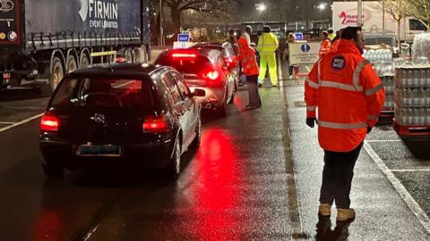 Queuing cars being loaded with bottled water with men wearing orange jackets with Southern Water logos